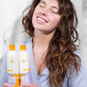 Woman with long, wavy hair holding two bottles of Earth Science fragrance-free shampoo and conditioner.
