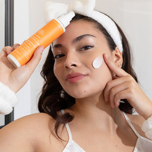 Woman applying moisturizer to her face with a bottle of Earth Science Almond-Aloe Moisturizer.