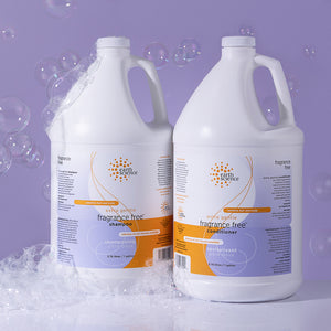 Two bottles of Earth Science fragrance-free shampoo and conditioner on a purple background with bubbles.