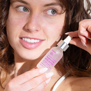 Woman applying the Earth Science Hyaluronic Acid skincare serum to her face with a dropper bottle.