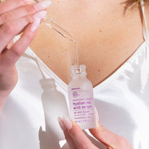 Person holding a bottle of hyaluronic acid serum with dropper over skin.