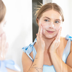 Woman applying cream to her face in front of a mirror
