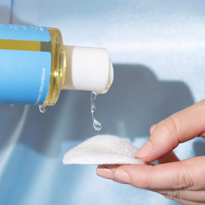 Bottle of Earth Science Aloe Vera Complexion Toner and Freshener skincare product being used on a cotton pad with a blue background