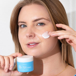 Woman applying night cream to her face with a jar of night cream in her hand.