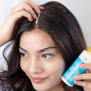 Woman applying hair product to her hair with a bottle of Earth Science Olive & Avocado hair and scalp care product.