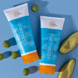 Two bottles of Earth Science olive and avocado hair care products on a blue background with avocados.