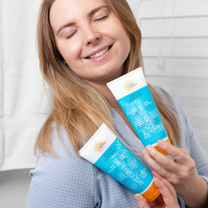 Woman holding two bottles of shampoo and conditioner with a neutral background