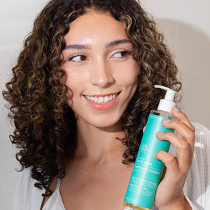 Woman holding a blue bottle with a pump, smiling against a neutral background