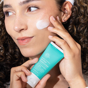 Woman applying a tube of clear skin cream to her face