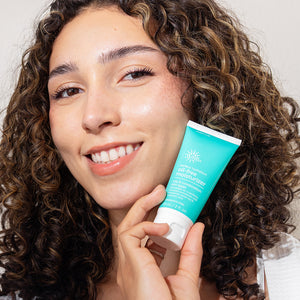 Woman holding a tube of moisturizer with a neutral background
